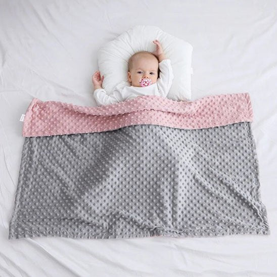 couverture bebe gris rose avec bulles en relief sur enfant allonge